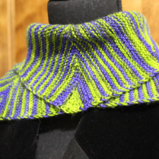 Cowl knit in high-contrast variegated yarn. Design has a miter that brings the front to a point.