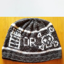 Colorwork hat with a piece of cake, the word or, and a skull and crossbones, echoing comedian Eddie Izzard’s Cake or Death routine.
