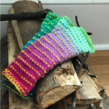 Fingerless mitts in a bright gradient with tiny bobbles every half-inch or so. Mitts are resting on a stack of firewood.