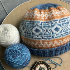 Colorwork beanie in cream, blue and gold, with hourglass motif bands and a ribbed edge.