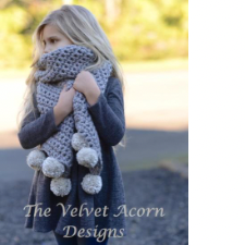Little girl wearing crocheted scarf that has several large pom-poms at each end.