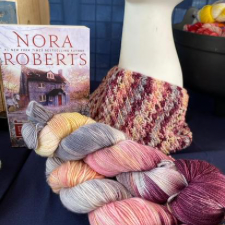 Cowl in starburst-style stitch, alongside variegated skeins and inspirational Nora Roberts book cover.