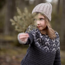 Child holding out a pine branch while wearing a two-color crochet sweater with a similar motif.