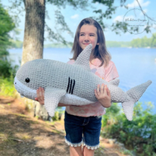 Child holds crocheted stuffed shark that is almost as large as she is.