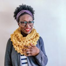 Smiling designer models bobbled crochet cowl.