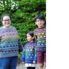 Colorwork sweaters on an adult and two children with rows of hearts and inverted hearts. Each row is a different rainbow color.