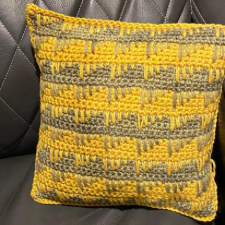 Two-color geometric crochet pillow where loops from the color above cross into the color below.