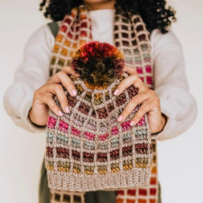 Tunisian crochet hat in two yarns. A neutral color forms a grid and a gradient yarn provides colorful squares. In the background is a matching scarf.