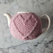 Tea cozy with traveling cable heart shape, filled with moss stitch.