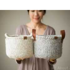 Woman holding two stiff baskets, one with leather handles, one with handles made of yarn.