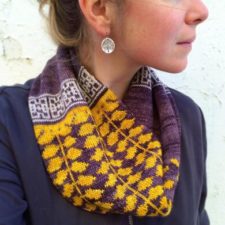 Cowl has colorwork of complex leaves, bordered by a geometric pattern.