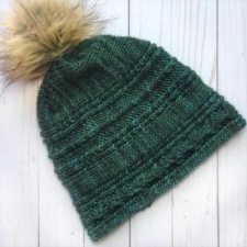 Cabled and textured slouchy hat. Pattern is in horizontal stripes of texture and has a pom-pom on top.