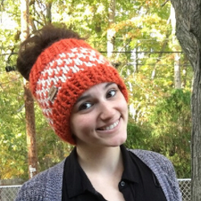 Knitted ear warmer or ponytail hat in bulky yarn in two colors. Top and bottom are ribbed in main color. Body is checked with contrasting color.
