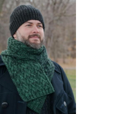 Smiling, bearded man wears scarf with interwoven cables.
