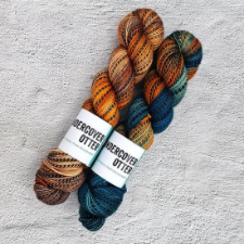 Two skeins of marled yarn, one in warm oranges and browns, the other in deep blue greens with splashes of warm oranges and browns.
