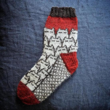 Colorwork socks of overlaid cat heads. The cats have only their ears and eyes showing.Cuffs, heels and toes add bright pops of solid color, and the soles are a diagonal colorwork grid.
