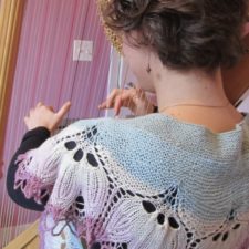 Woman playing harp, wearing semicircular shawl with deep floral border. Yarn is a soft multicolor gradient.