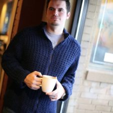 Man wearing textured zip cardigan holds cup of tea.