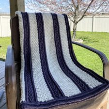 Crocheted blanket with vertical stripes that vary in color and texture.