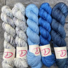 Five skeins, with two speckled off-white skeins, and three semisolid blues in different shades.