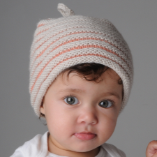 Darling hazel-eyed baby wears hat with knits in one color, purls in another, and a tiny loop at the top.