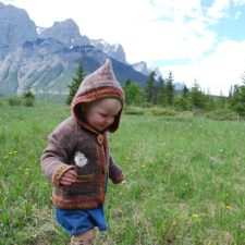 Toddler in hooded button-up cardigan that has contrasting linen stitch bands around hood, hem, button band and cuffs.