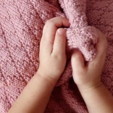 Toddler hands squish knitted blanket in simple pattern of rhombus/diamond texture.