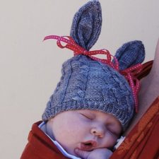 Baby in hat that has bunny ears and cables.