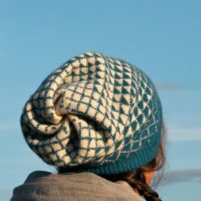 Slouch hat has two color design in angled grid that shifts from one color to the other along the length of the hat. The slouchy part at the top joins in a swirl of knitted fabric.
