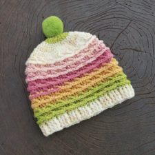 Hat with color bands that look like frosting swirls. hat has small pom-pom on top and ribbed brim.