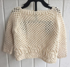 Baby sweater knitted with lots of openwork, and a shell border at the hem.