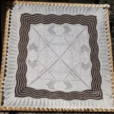 Square lace blanket, knit center outward with geometric pattern.