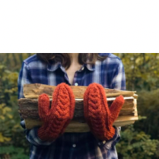 Woman wearing mittens with staghorn cables up the middle. In her arms is firewood.