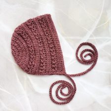 Crocheted bonnet with textured stripes and long, thin ties.