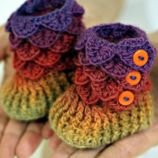 Tiny crocheted booties with overlapping dragon scales on the legs and tiny button down the outside edge.