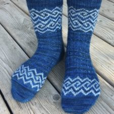 Socks with geometric key-style colorwork in a band across the toes and around the calf.