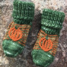 Child’s socks in the colors of pumpkin fruit and leaves, with small pumpkin motifs on top of the foot.