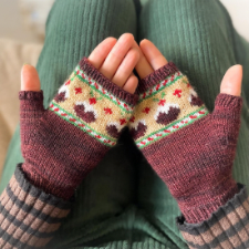 Colorwork fingerless mitts with band of candy cane stripes and Christmas puddings across the body of the hand.