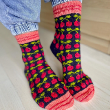 Socks have striped cuffs and toes. Body of the sock is bright colorwork cherries on steps against a dark background.
