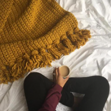 Uniform crocheted blanket in chunky yarn, with plump tassels along the edge.