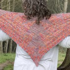 Triangular shawl has two sets of cables that extend from each lower edge toward the center. They rise in several cabled peaks.