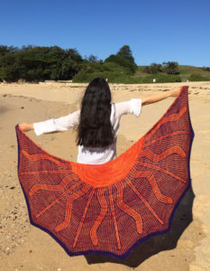 Woman on the beach holds large shawl with a sun design.