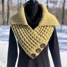 Crisscrossed cowl with folded down collar. Cowl has a waffle texture and is buttoned along one edge.
