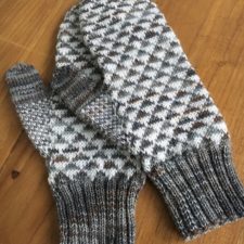 Mittens with solid color ribbing at wrist, geometric pattern in two colors with tiny triangles on body, and single color thumb.