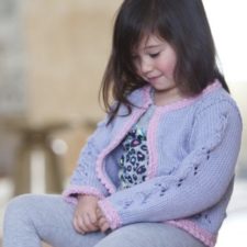 Child wears sweater with lacy cable detail down sleeves and contrasting hem, neck and button bands.