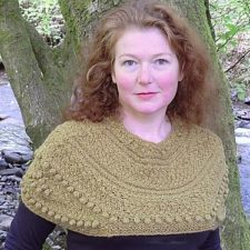 Designer Sally Pointer wears a beautiful bobbled shawl. In the background is a large tree.