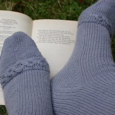 Open copy of Lord of the Rings book, and feet wearing socks that have a cabled ring right before the toe.