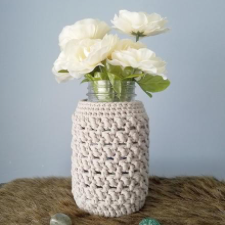 Glass jar covered in textured crochet. Jar is filled with large, white flowers.