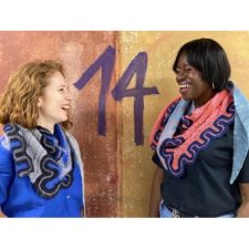 Two women laugh, wearing the wavy-edge colorful shawl in different colorways.