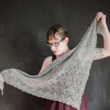 Designer extends her arms to show off triangular shawl featuring classic lace, finished off with an easy garter border.